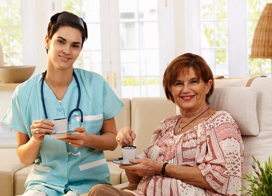nurse and senior woman are having a cup of tea while smiling